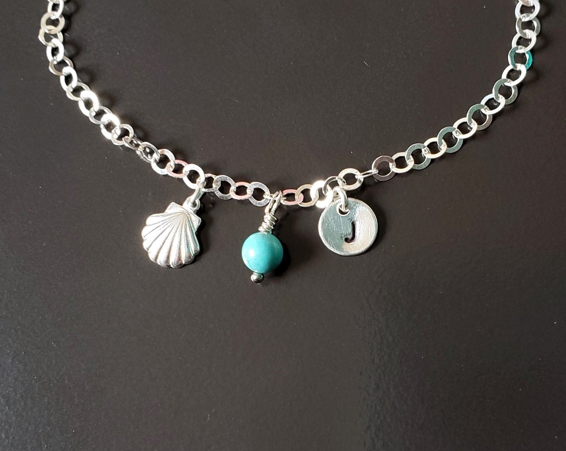 Deluxe Personalized Anklet-Ankle Bracelet, a shell, an round initial pendant and Turquoise birthstone pendant dangle from sparkly sterling silver chain, displayed on black background. 