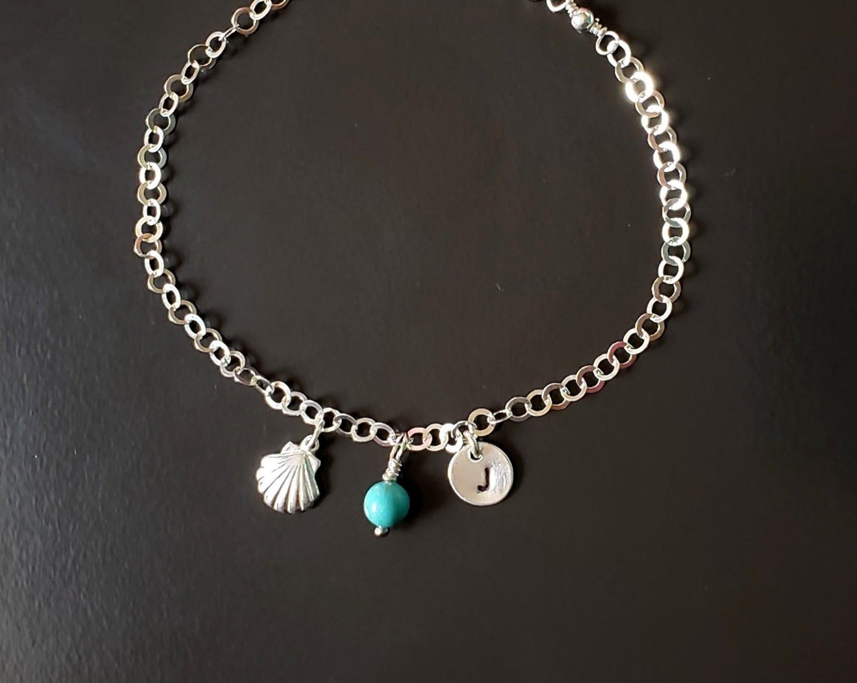Deluxe Personalized Anklet-Ankle Bracelet, a shell, an round initial pendant and Turquoise birthstone pendant dangle from sparkly sterling silver chain, displayed on black background.