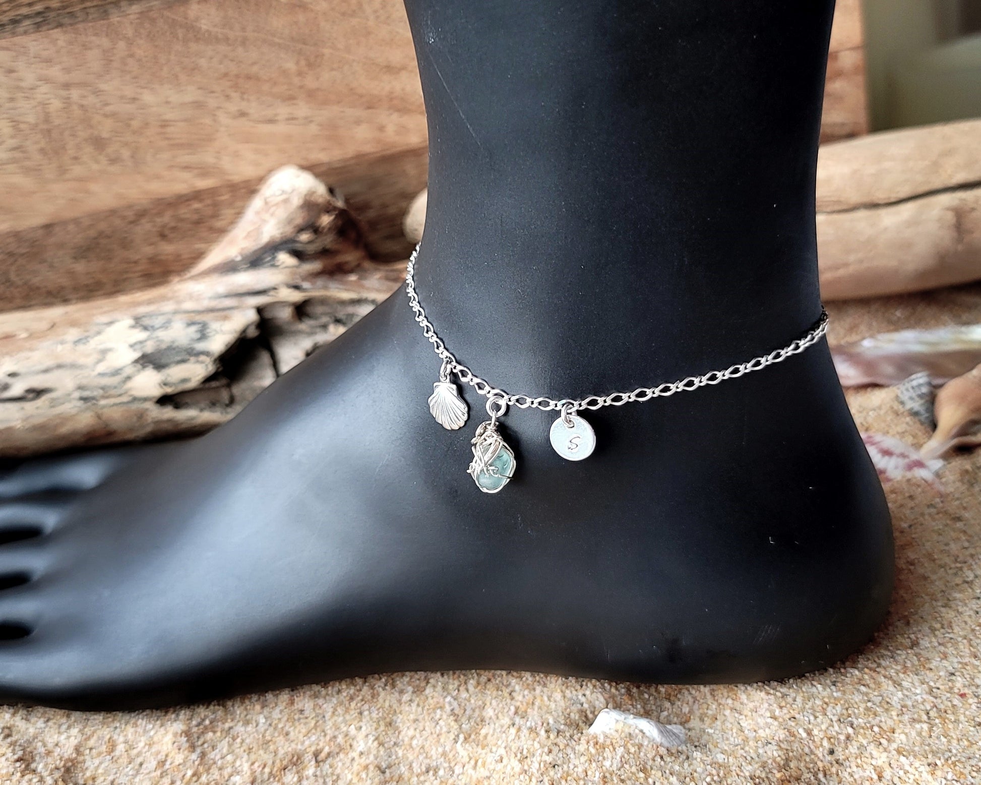 Silver Anklet with Fancy Chain and dangling Shell, Aqua Blue Beach Glass wire wrapped pendant and round disk shaped initial pendant on wood and sand background 