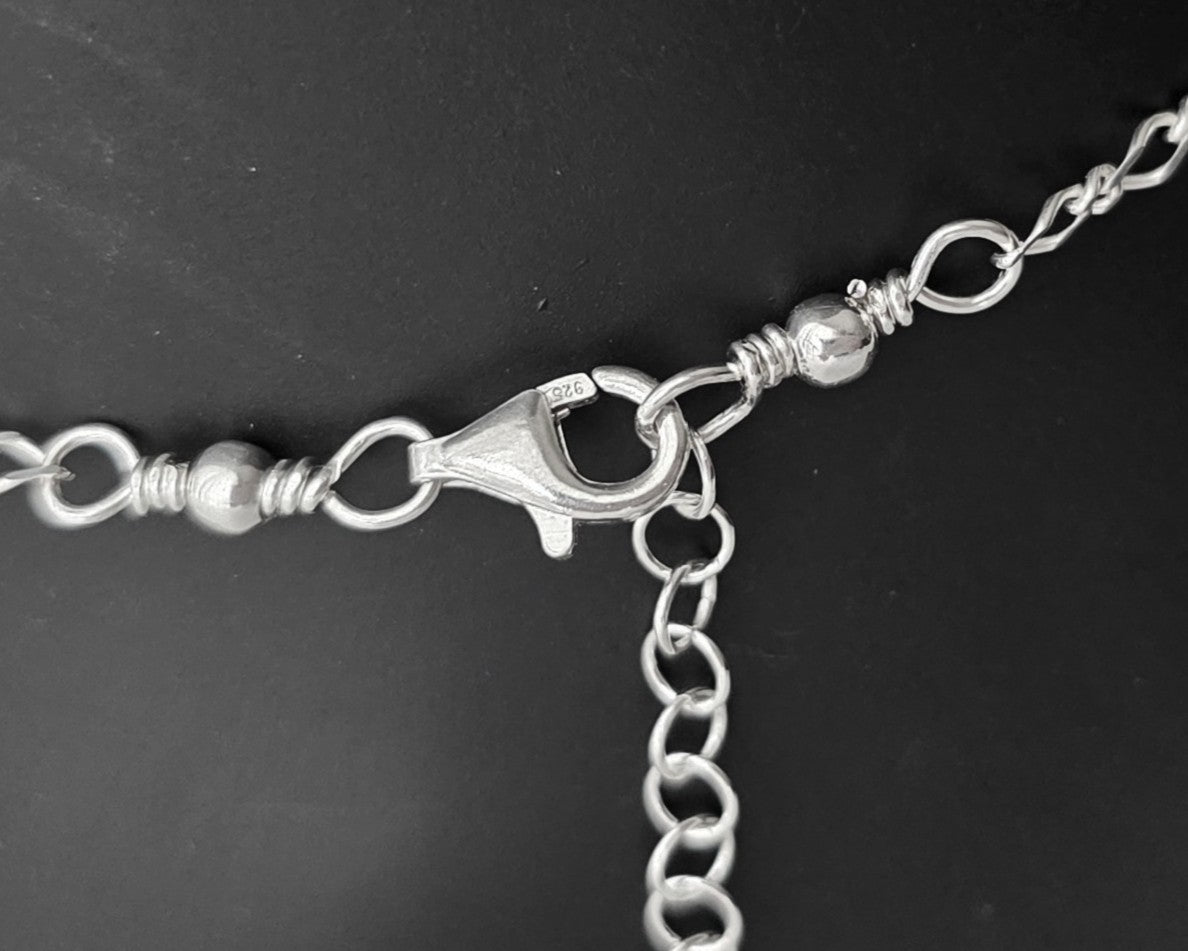 Close Up of Lobster Claw Clasp, Eternity Coil pendant, flat figaro chain on black background 
