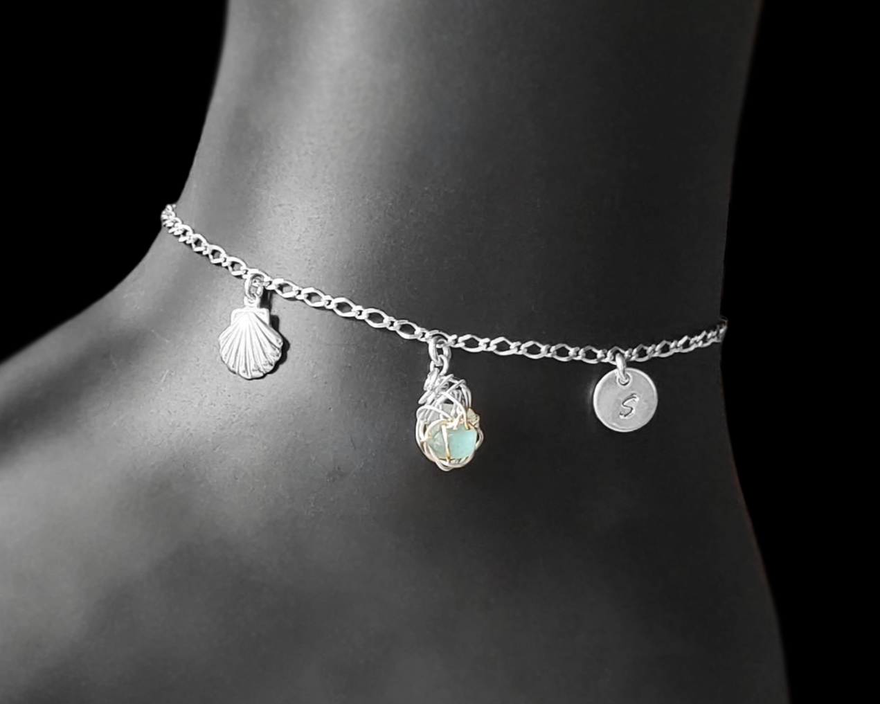 Sterling Silver Aqua Blue Beach Glass/ Sea Glass Anklet, Ankle Bracelet with a Shell, round Initial pendant and Celtic Eternity Coil pendant on flat figaro chain on black background 
