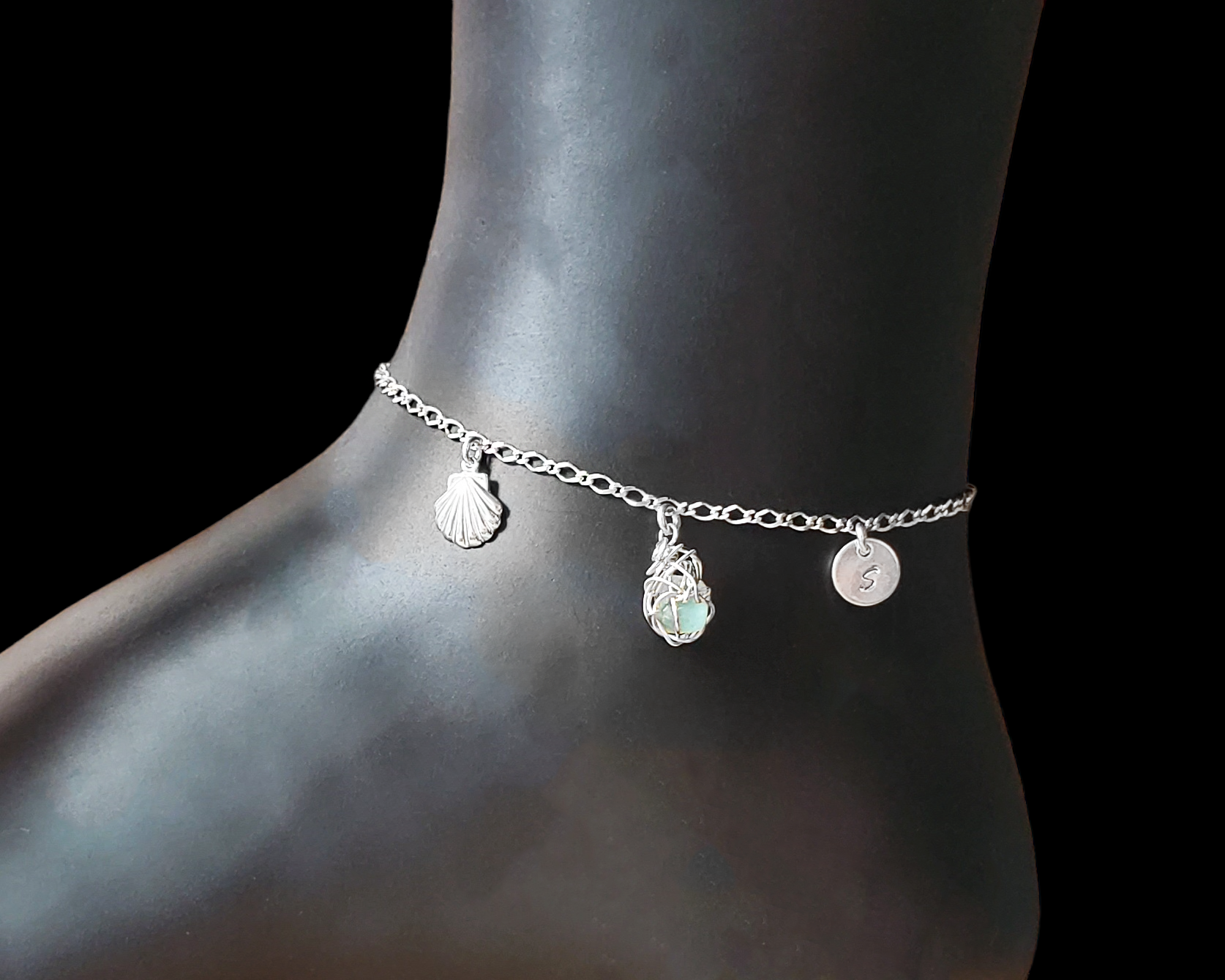 Sterling Silver Aqua Blue Beach Glass/ Sea Glass Anklet, Ankle Bracelet with a Shell, round Initial pendant and Celtic Eternity Coil pendant on flat figaro chain on black background 