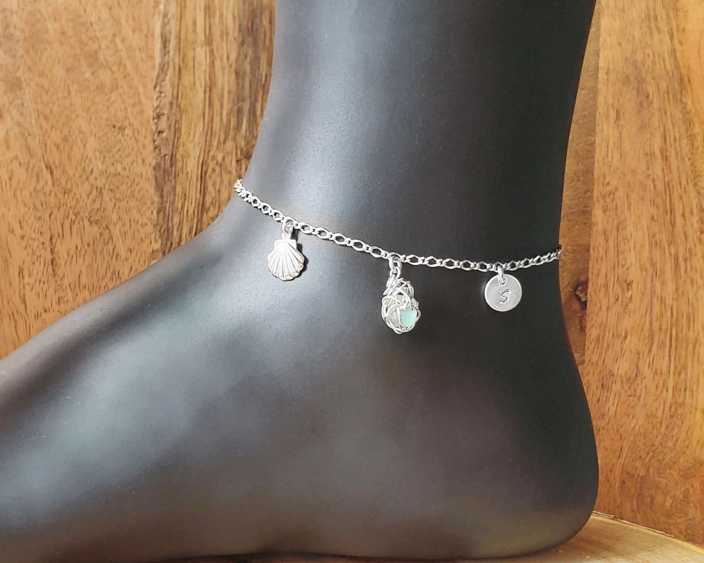 Sterling Silver Aqua Blue Beach Glass/ Sea Glass Anklet, Ankle Bracelet with a Shell, round Initial pendant and Celtic Eternity Coil pendant on flat figaro chain on wood background 