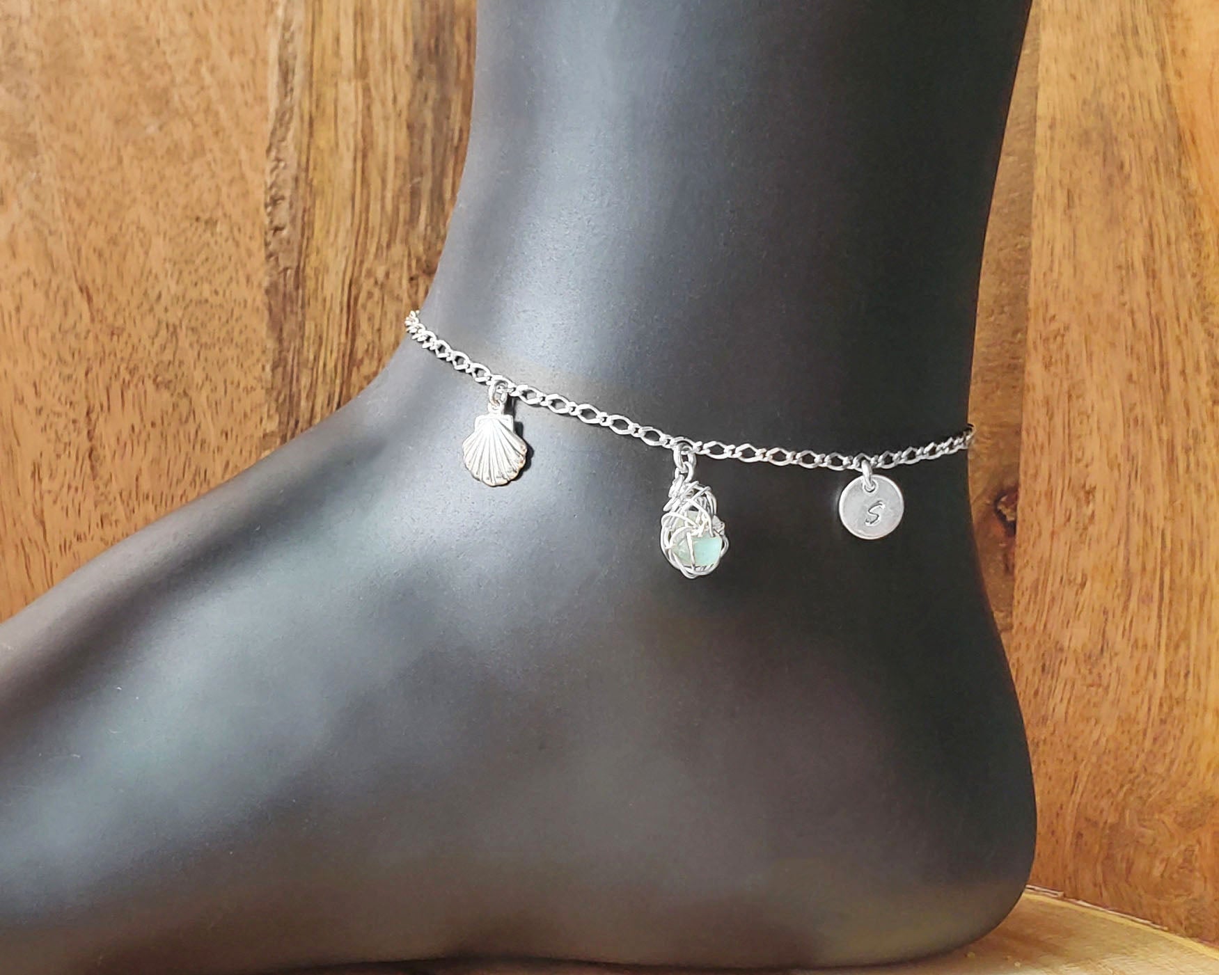 Sterling Silver Aqua Blue Beach Glass/ Sea Glass Anklet, Ankle Bracelet with a Shell, round Initial pendant and Celtic Eternity Coil pendant on flat figaro chain on wood background 