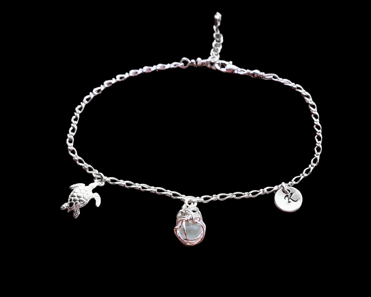 Sterling Silver Aqua Blue Beach Glass/ Sea Glass Anklet, Ankle Bracelet with a Turtle, round Initial pendant and Celtic Eternity Coil pendant on flat figaro chain on black background 