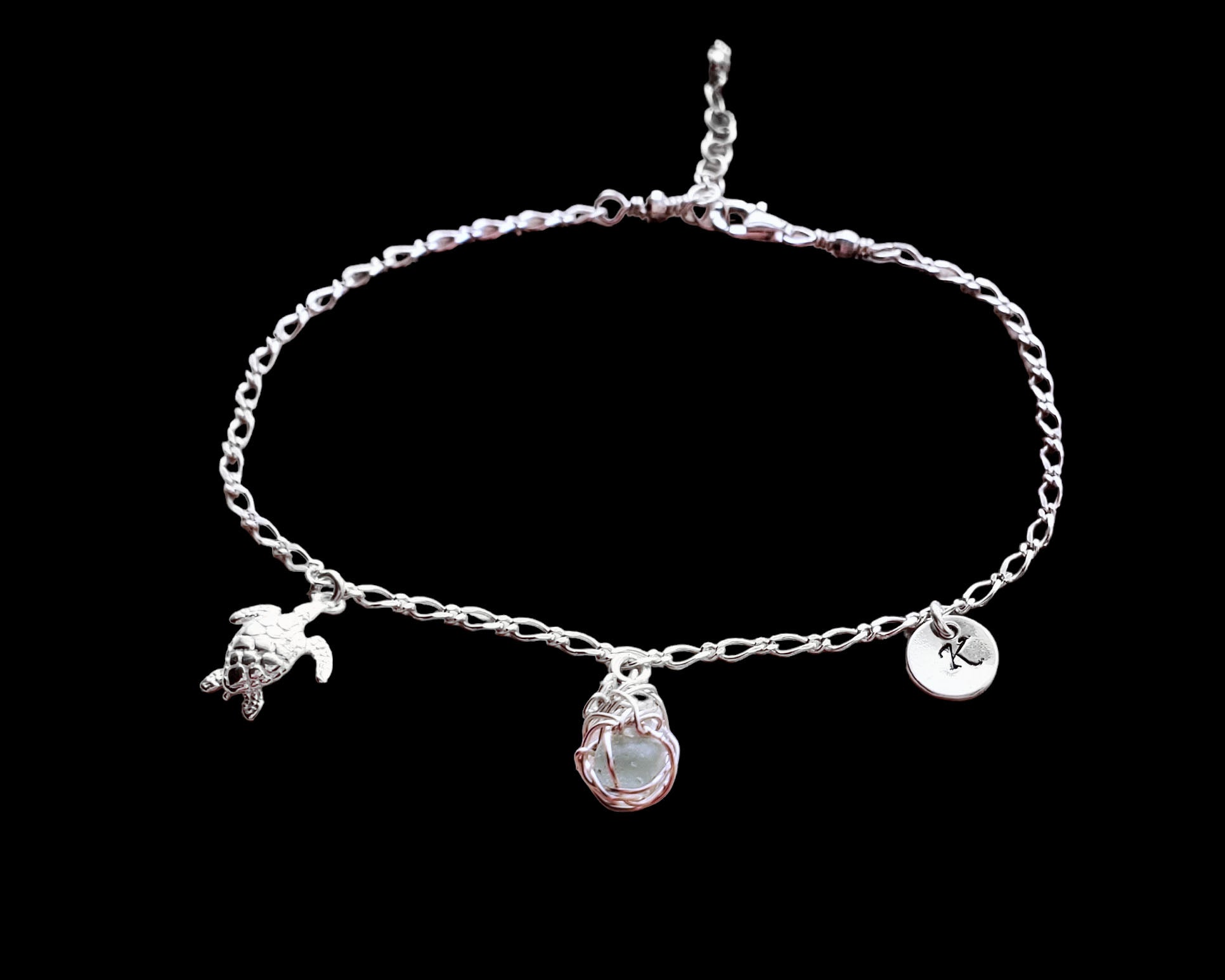 Sterling Silver Aqua Blue Beach Glass/ Sea Glass Anklet, Ankle Bracelet with a Turtle, round Initial pendant and Celtic Eternity Coil pendant on flat figaro chain on black background 