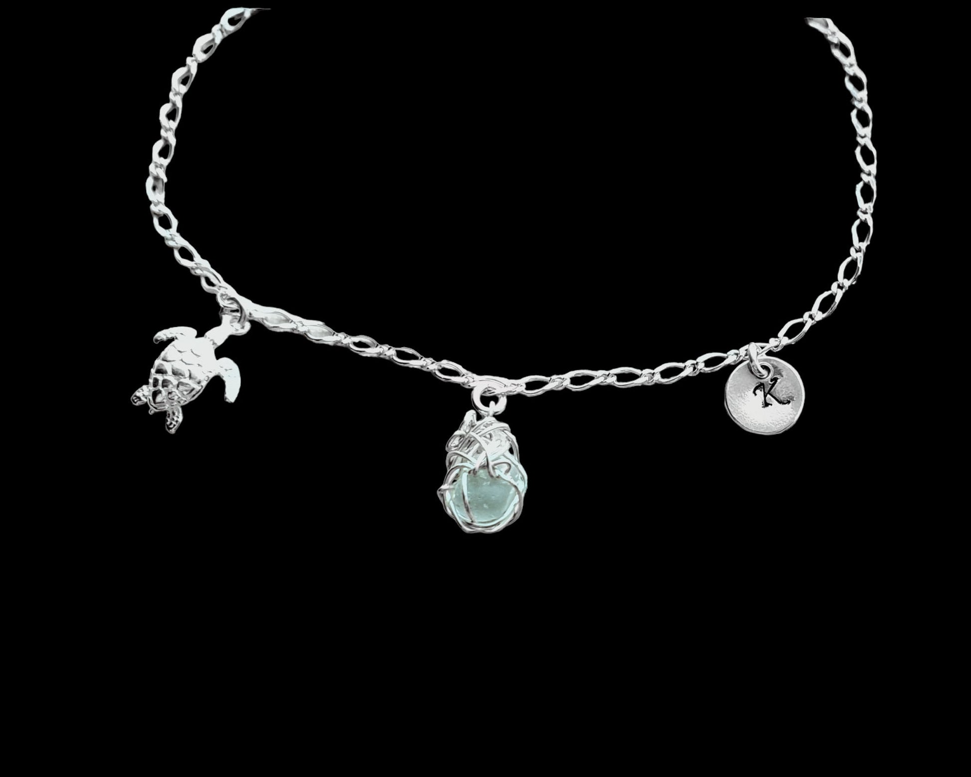 Sterling Silver Aqua Blue Beach Glass/ Sea Glass Anklet, Ankle Bracelet with a Turtle, round Initial pendant and Celtic Eternity Coil pendant on flat figaro chain on black background 