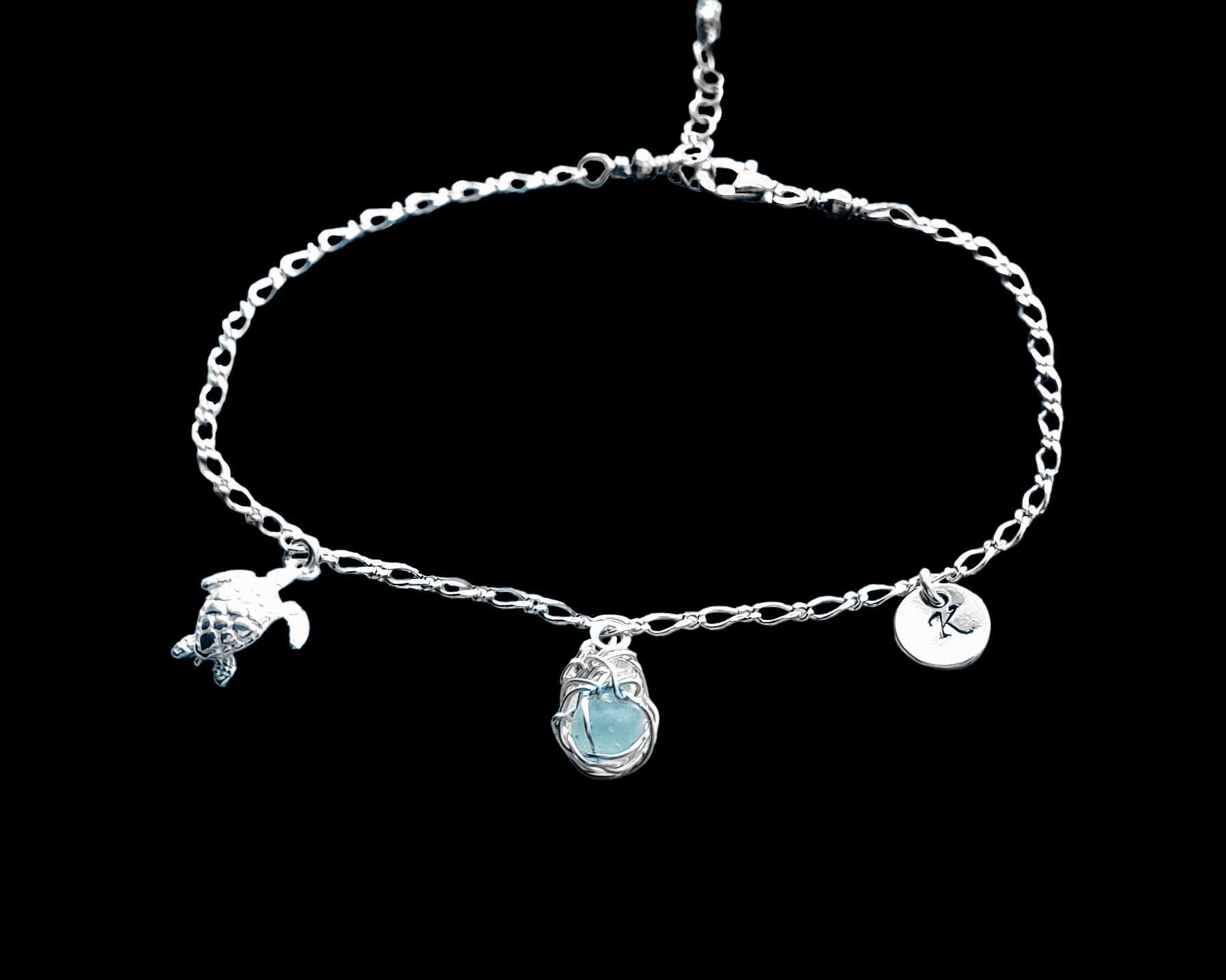 Sterling Silver Aqua Blue Beach Glass/ Sea Glass Anklet, Ankle Bracelet with a Turtle, round Initial pendant and Celtic Eternity Coil pendant on flat figaro chain on black background 