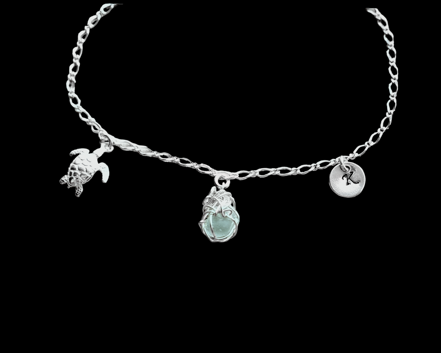 Sterling Silver Aqua Blue Beach Glass/ Sea Glass Anklet, Ankle Bracelet with a Turtle, round Initial pendant and Celtic Eternity Coil pendant on flat figaro chain on black background 