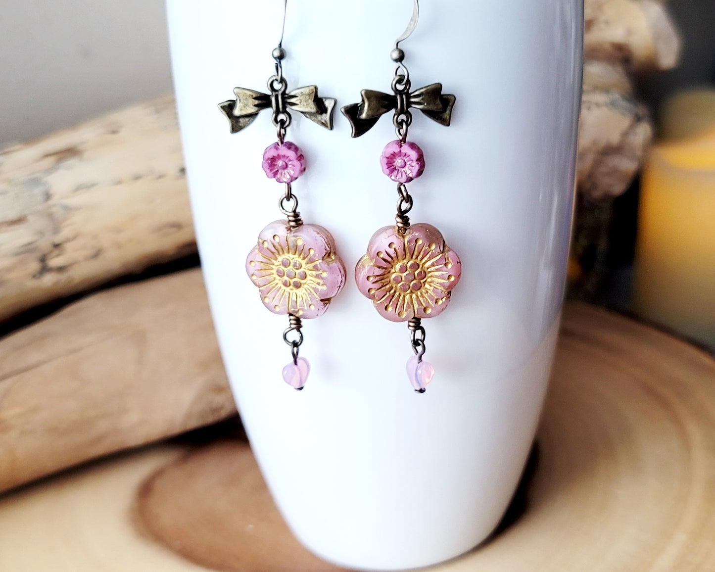 Long Vintage Romance Pink Flower Bow Earrings, with little pink heart dangles on the base, displayed on white cup
