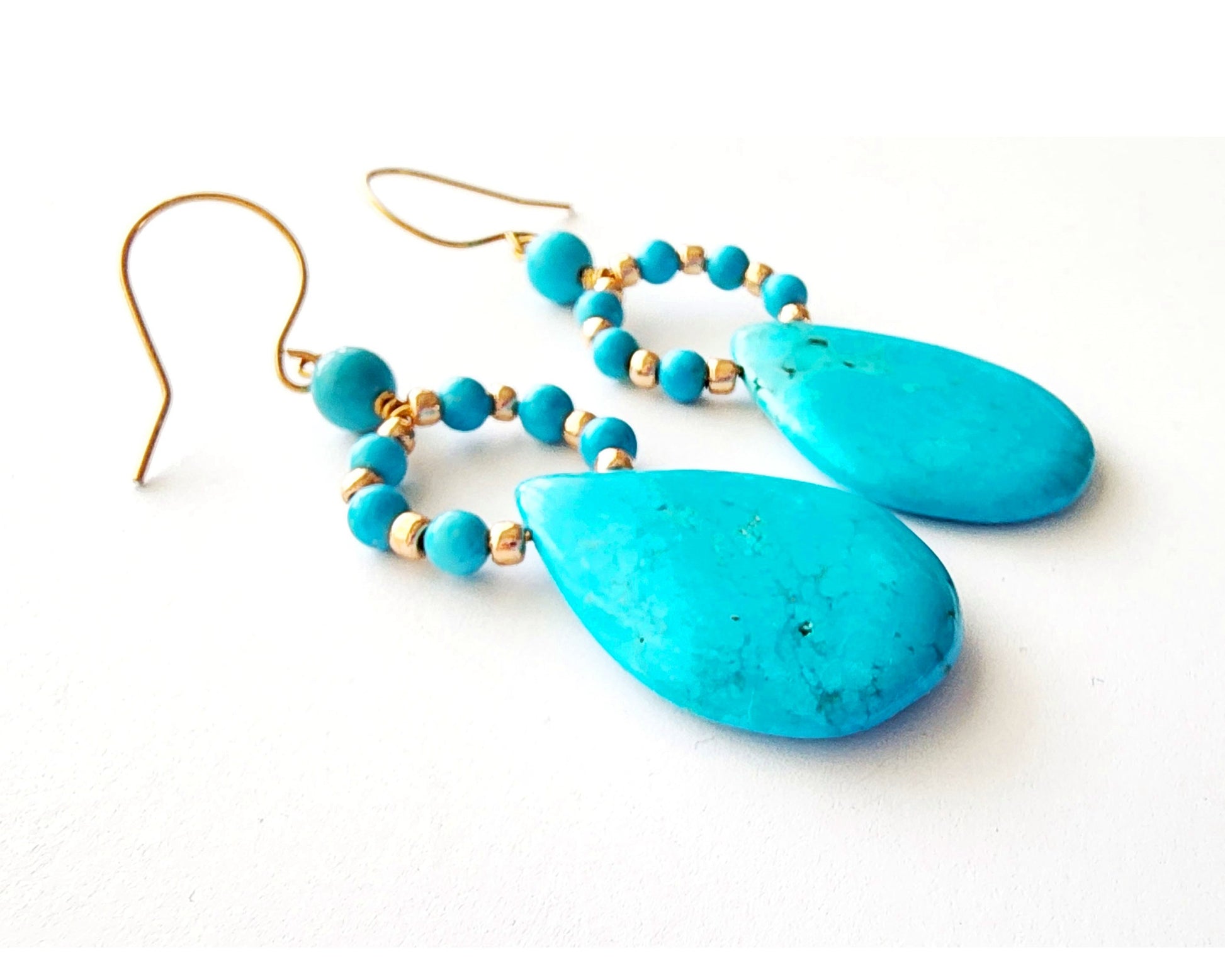 Long turquoise blue drop shape hoop dangle earring with large drop shape stones and gold wire and french earring hooks on white background