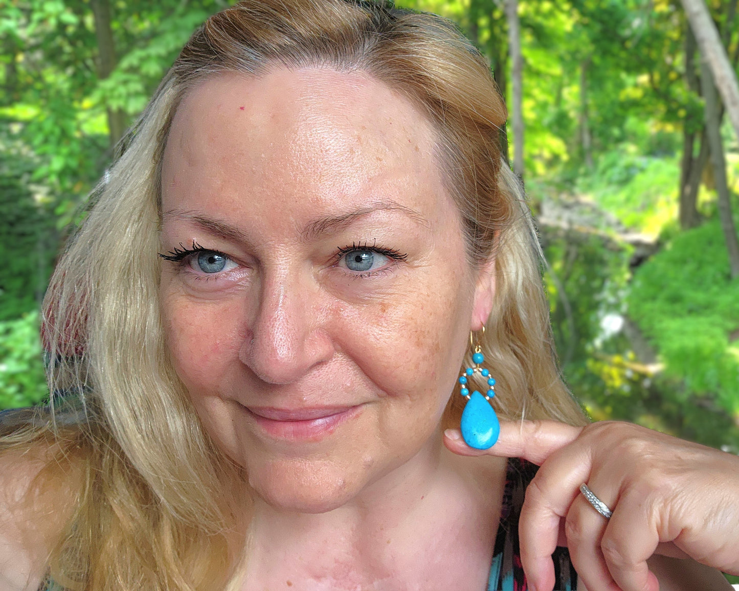 Woman wearing Long turquoise blue drop shape hoop dangle earrings outdoors with tree's 
