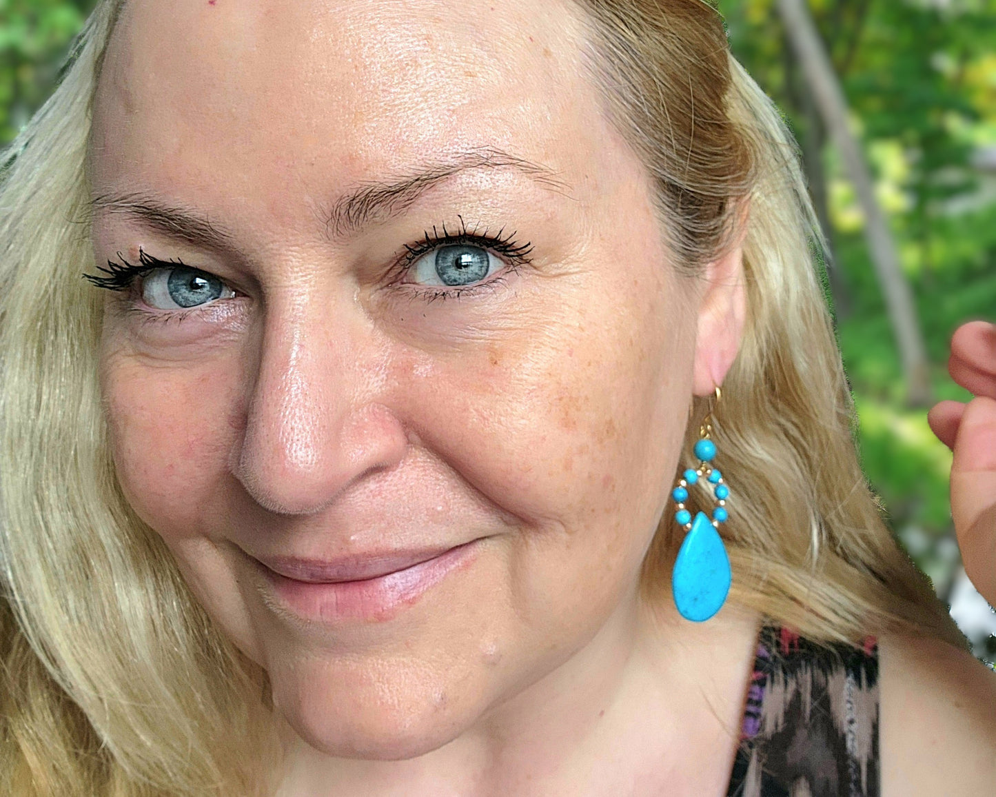 Woman wearing Long turquoise blue drop shape hoop dangle earrings outdoors with tree's 