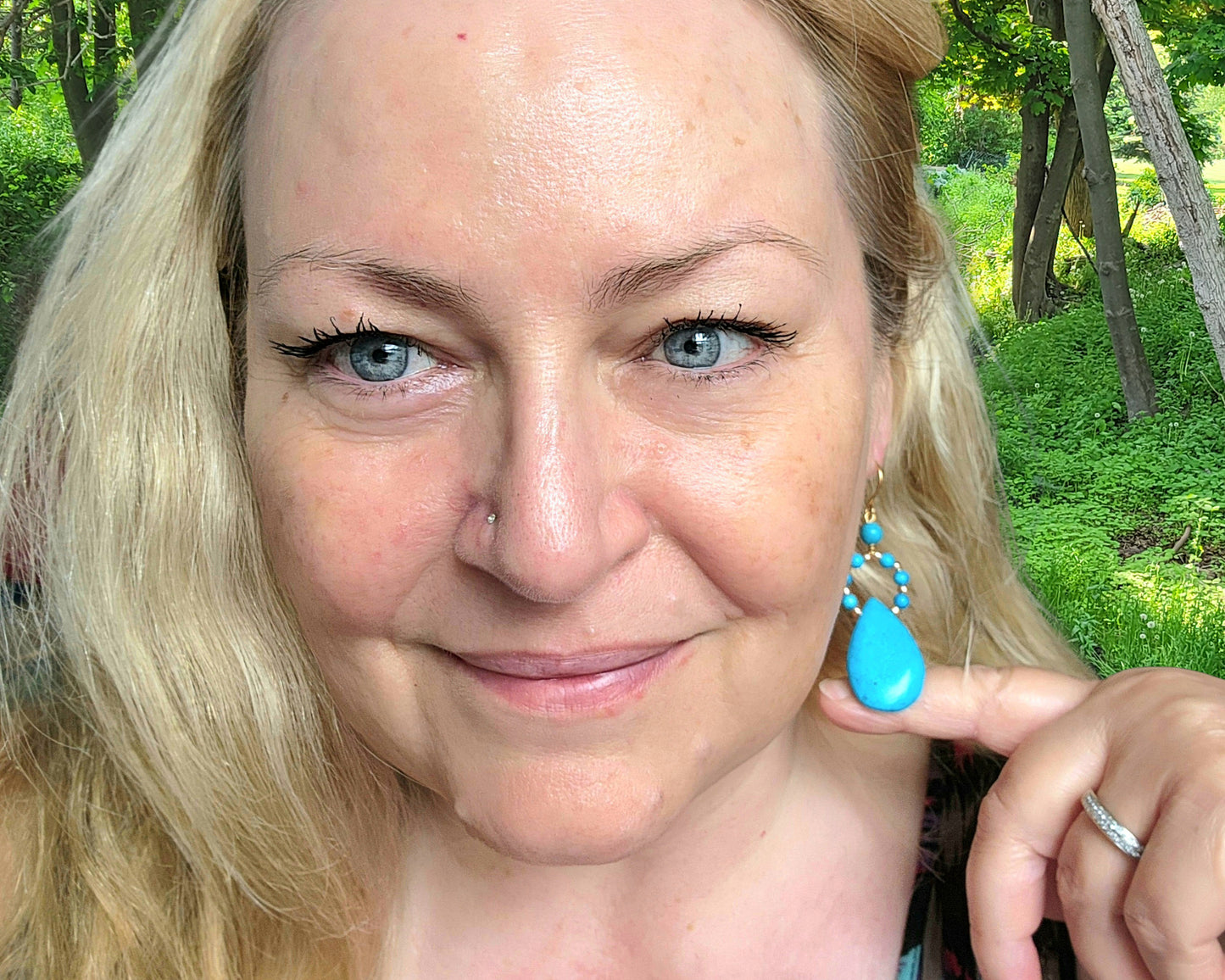Woman wearing Long turquoise blue drop shape hoop dangle earrings outdoors with tree's 