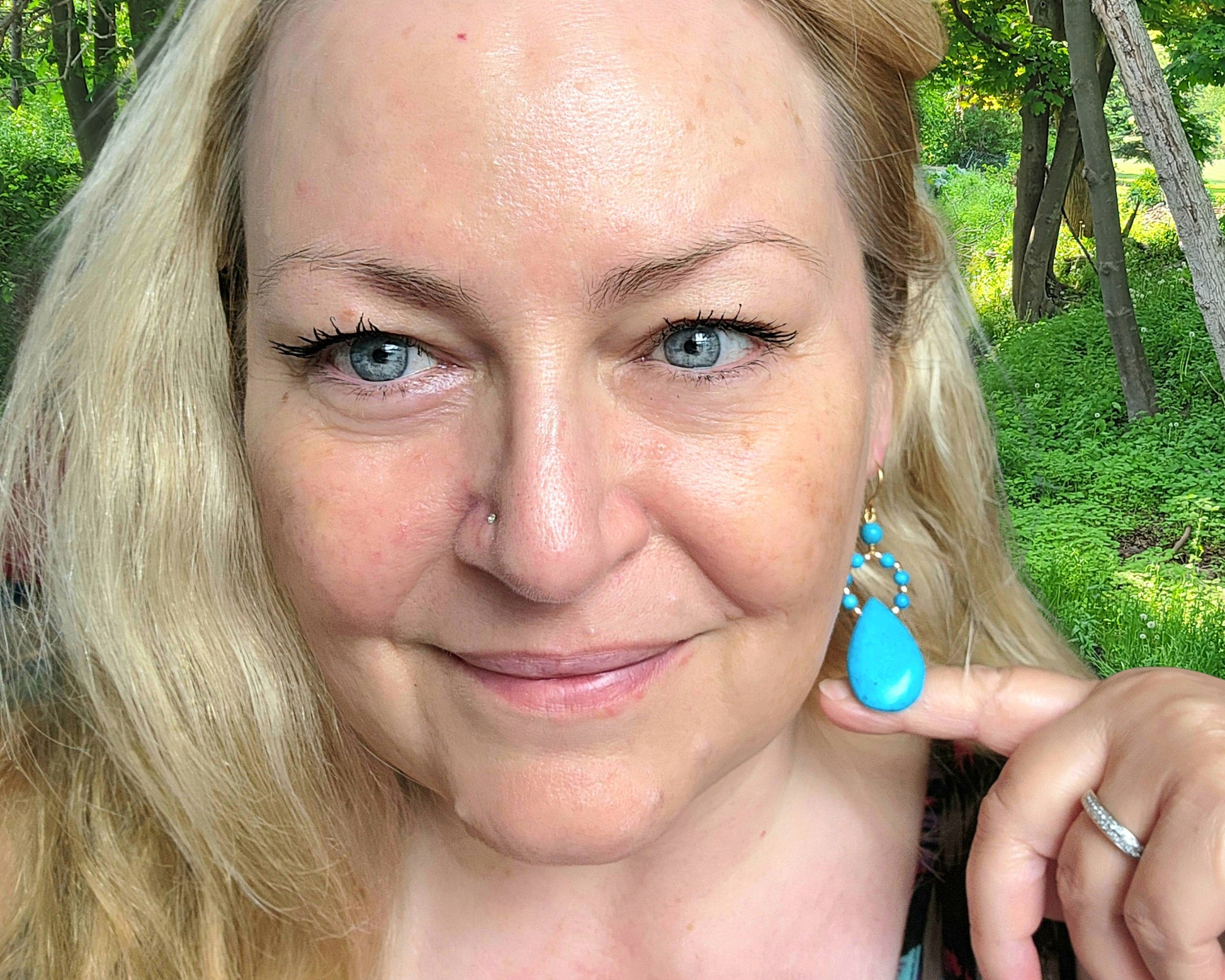 Woman wearing Long turquoise blue drop shape hoop dangle earrings outdoors with tree's 