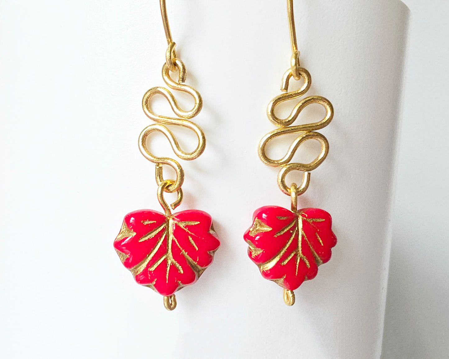 Gold Earrings with Swirling design and dangling red maple leaf’s with gold detail on white background