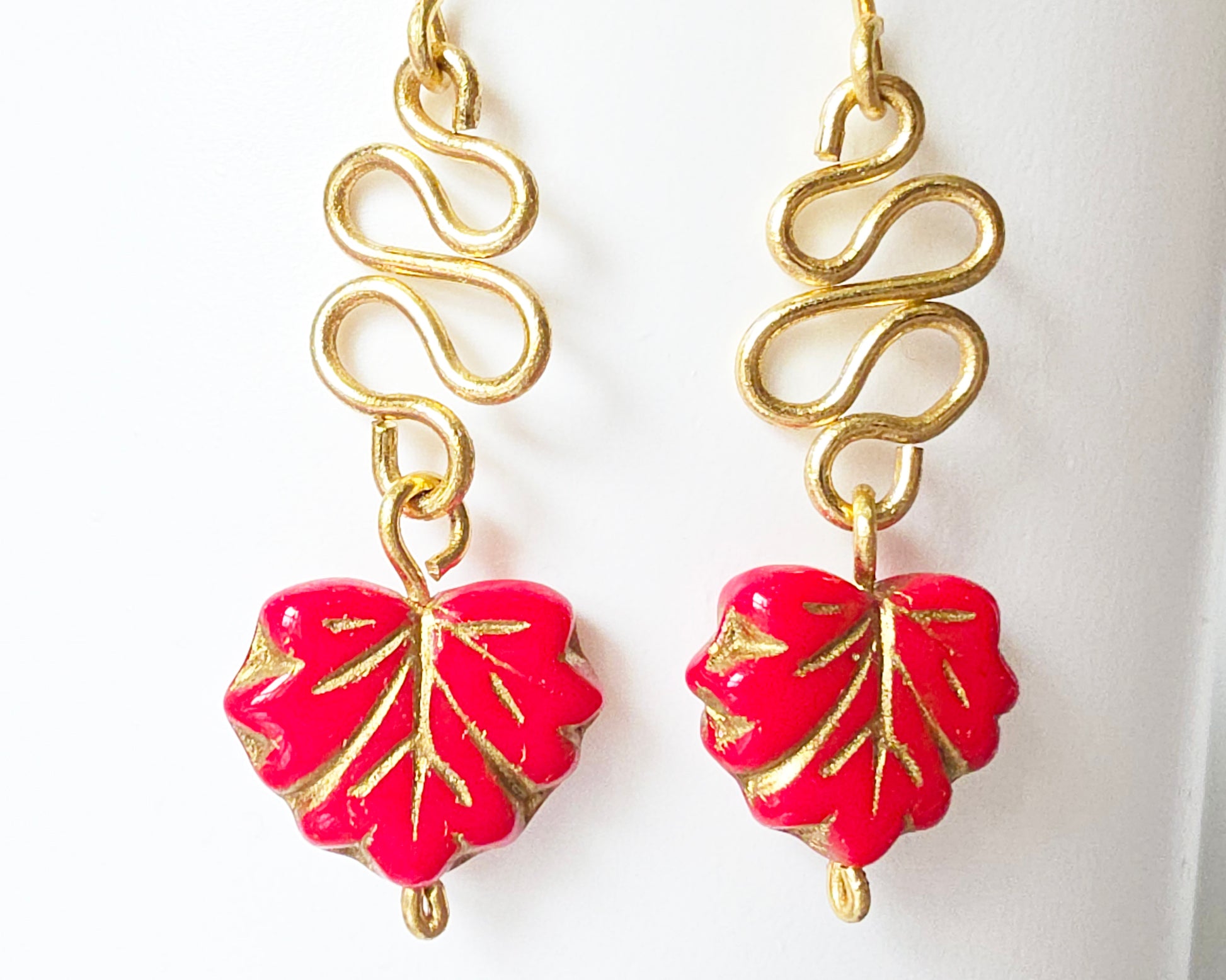 Gold Earrings with Swirling design and dangling red maple leaf’s with gold detail on white background