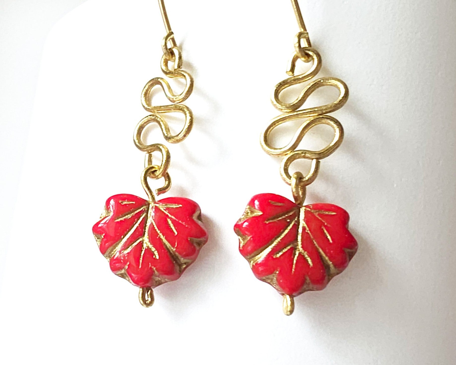 Gold Earrings with Swirling design and dangling red maple leaf’s with gold detail on white background