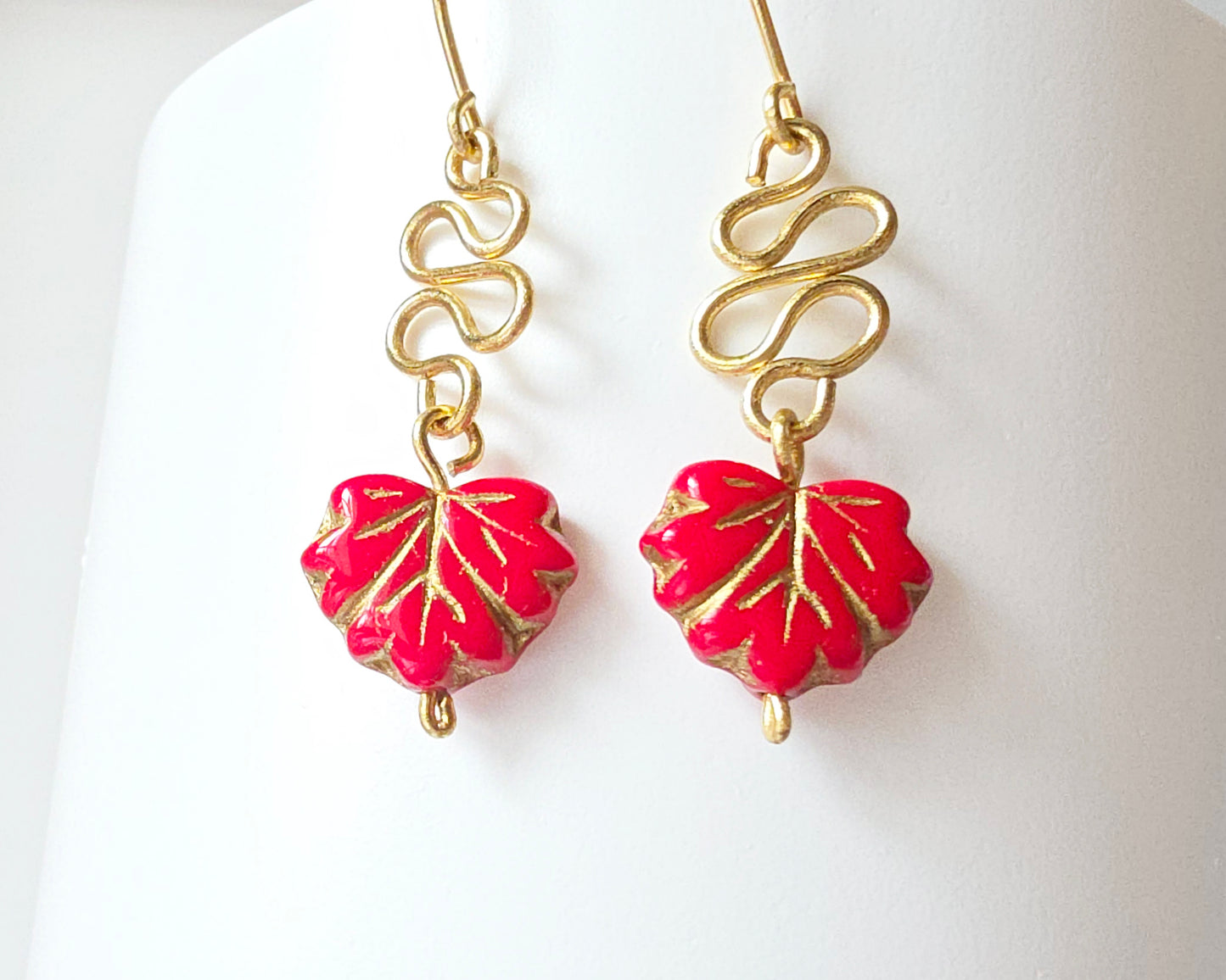 Gold Earrings with Swirling design and dangling red maple leaf’s with gold detail on white background
