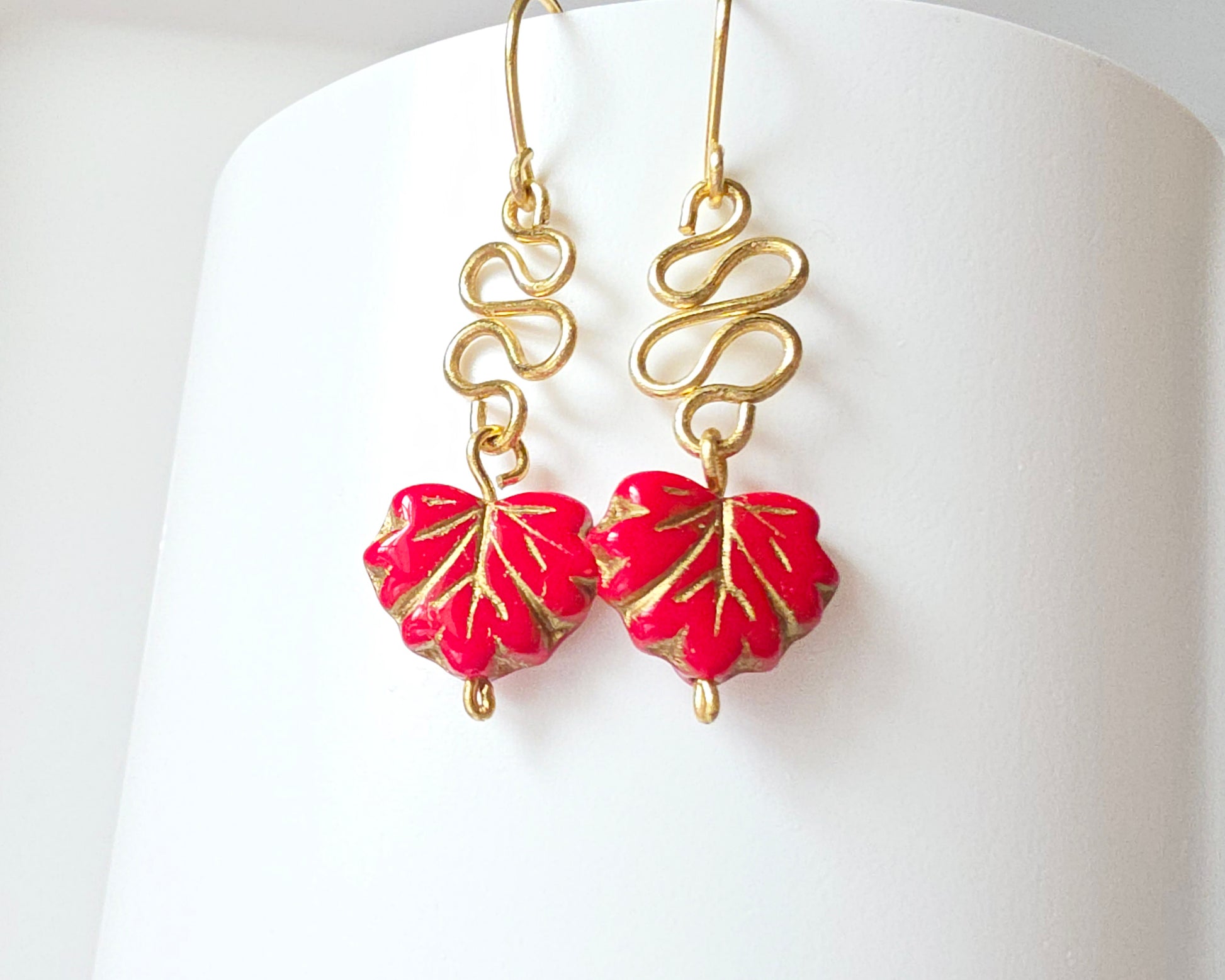 Gold Earrings with Swirling design and dangling red maple leaf’s with gold detail on white background