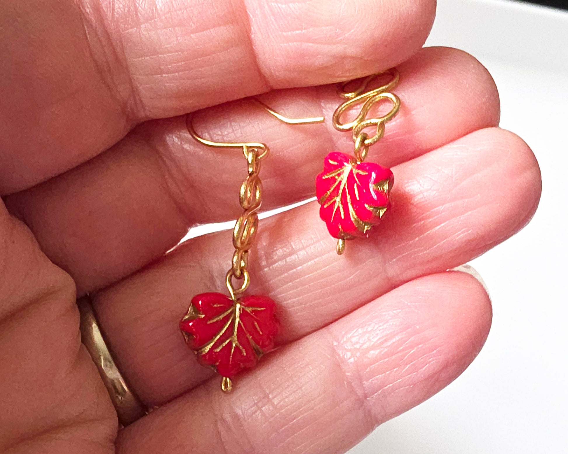 Gold Earrings with Swirling design and dangling red maple leaf’s with gold detail on hand 