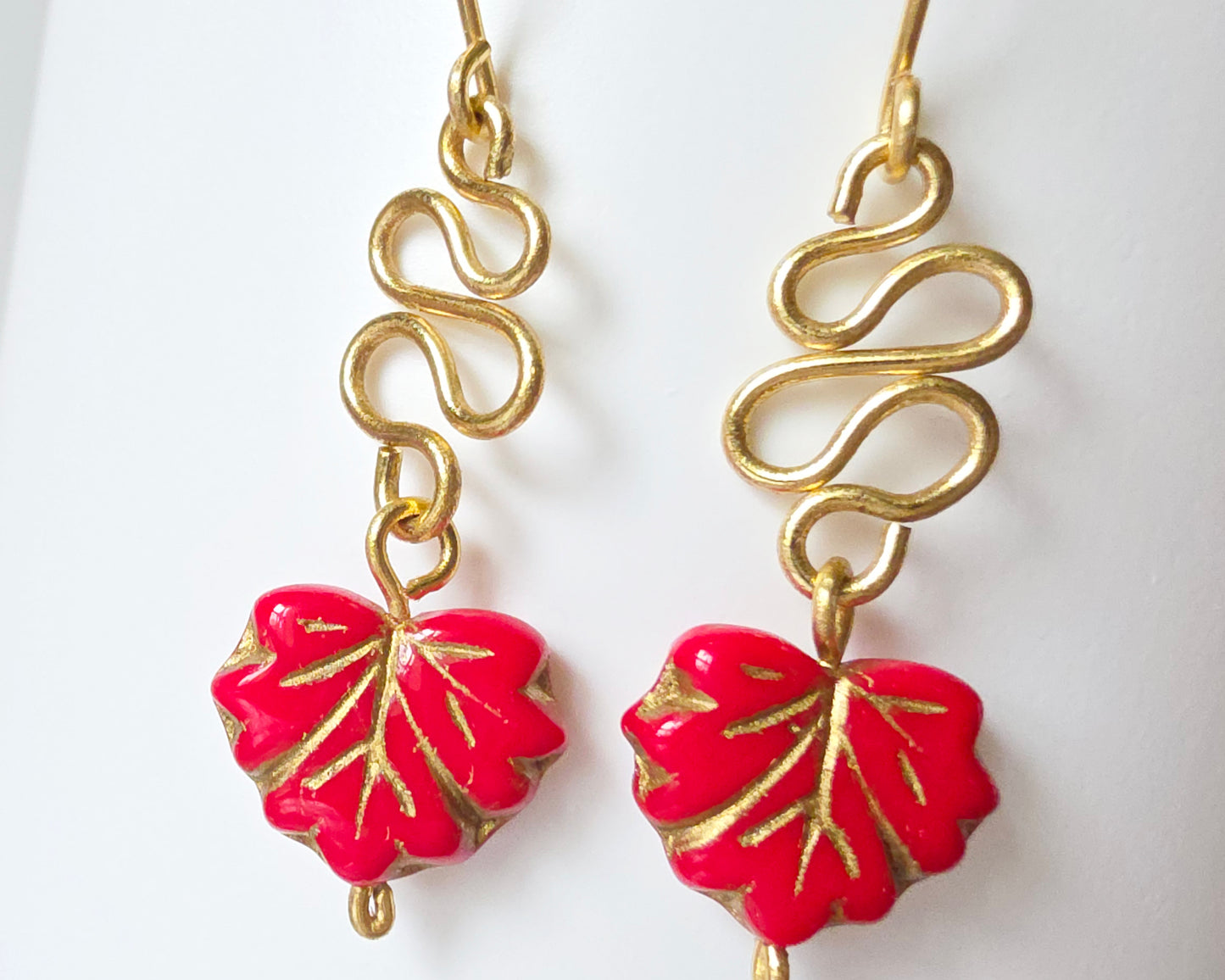 Gold Earrings with Swirling design and dangling red maple leaf’s with gold detail on white background