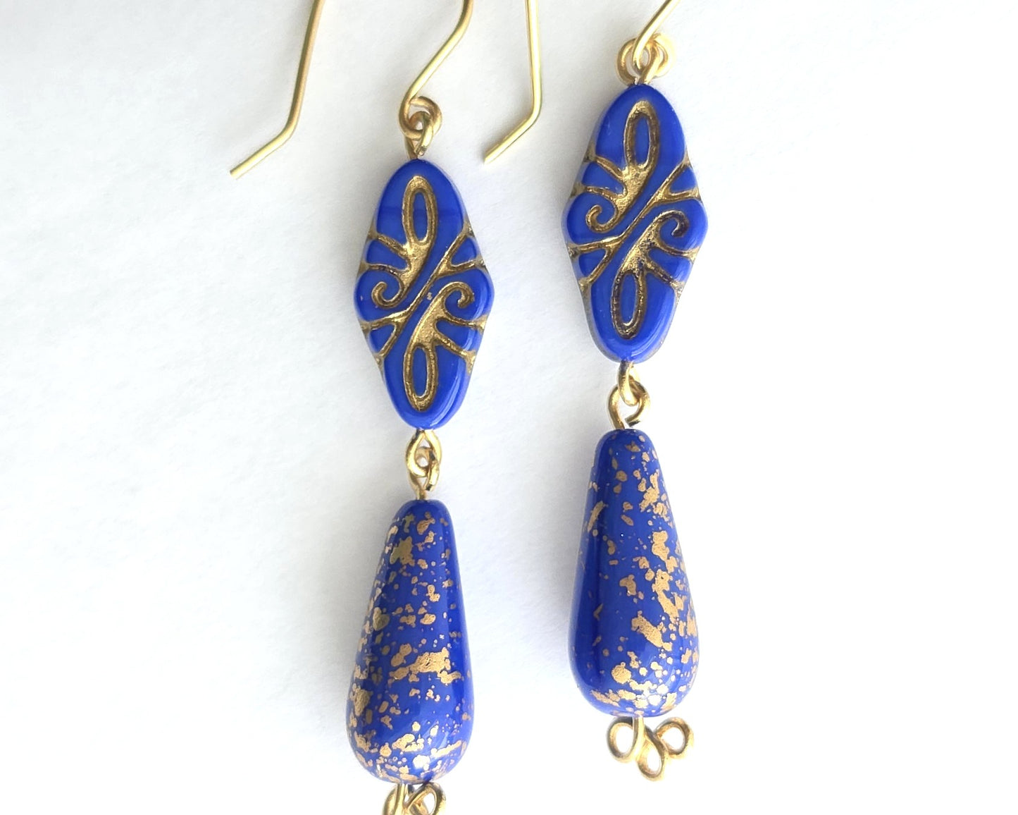 Pair of Art Deco style long blue earrings with gold detail and trinity knots on the base of the earrings with french style earring wires on white background 