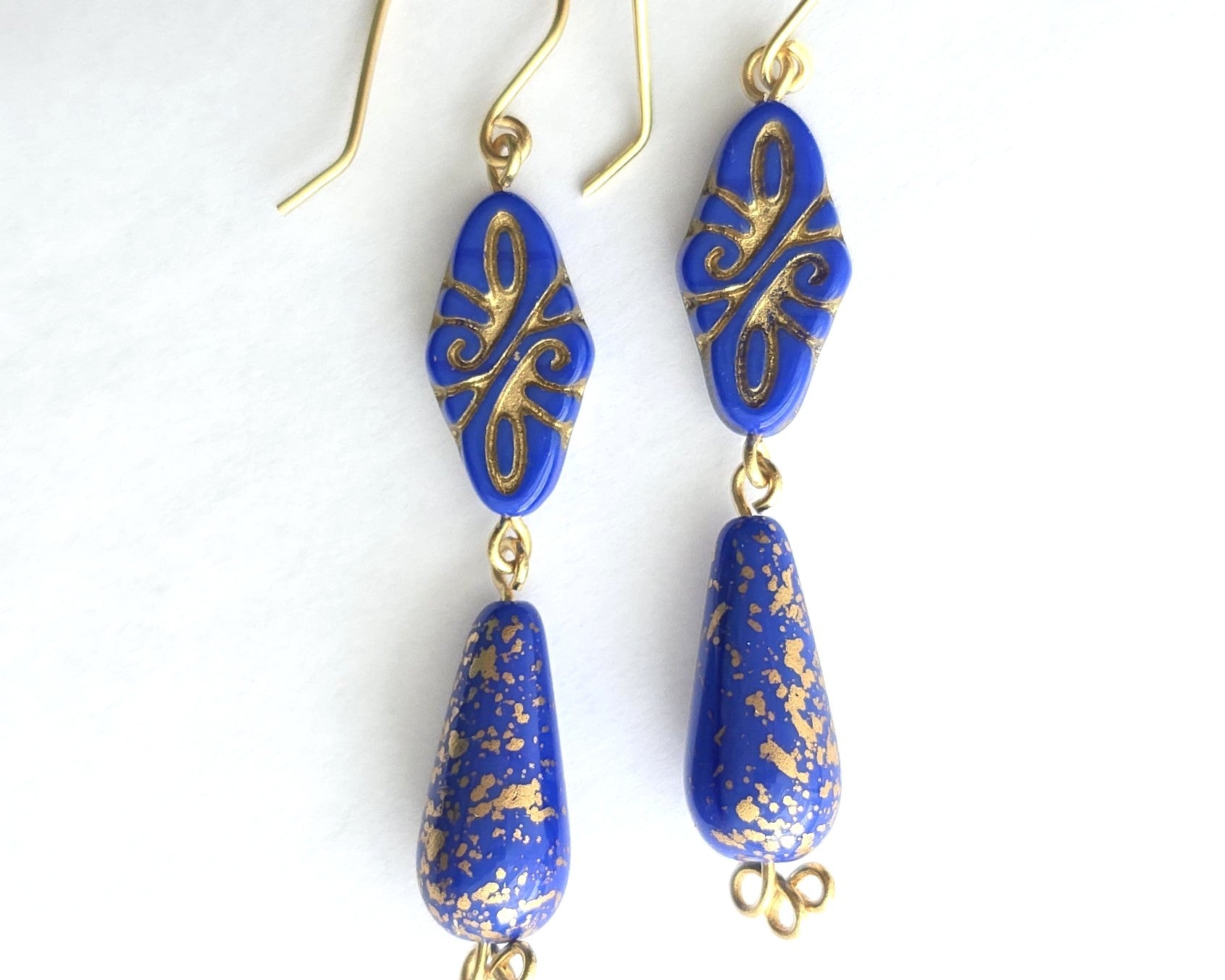 Pair of Art Deco style long blue earrings with gold detail and trinity knots on the base of the earrings with french style earring wires on white background 