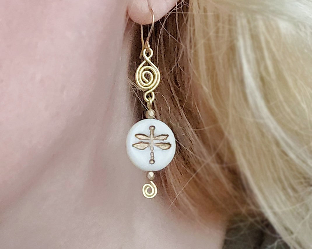 Gold and white dragonfly earrings with Celtic Coils and french style earring hooks worn by a person with blonde hair.