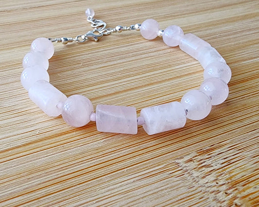 Rose Quartz PEACE bracelet, Morse Code spells the word PEACE with round and tube shaped pale pink Rose Quartz beads with Sterling Silver lobster claw clasp and extension chain, displayed on wood.