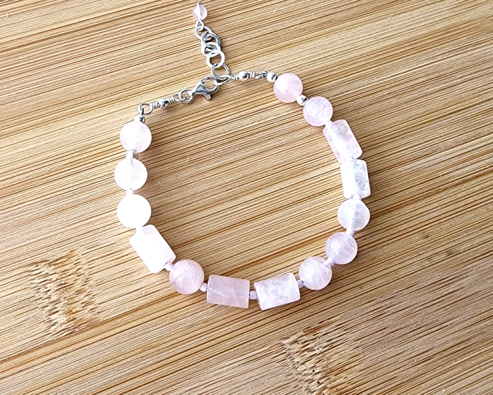 Rose Quartz PEACE bracelet, Morse Code spells the word PEACE with round and tube shaped pale pink Rose Quartz beads with Sterling Silver lobster claw clasp and extension chain, displayed on wood.