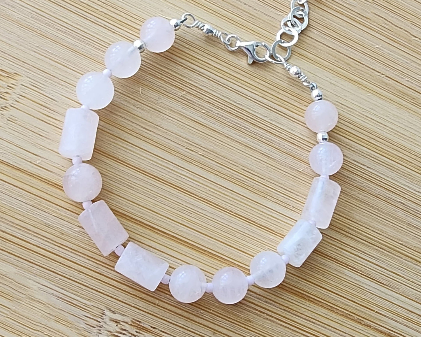 Rose Quartz PEACE bracelet, Morse Code spells the word PEACE with round and tube shaped pale pink Rose Quartz beads with Sterling Silver lobster claw clasp and extension chain, displayed on wood.