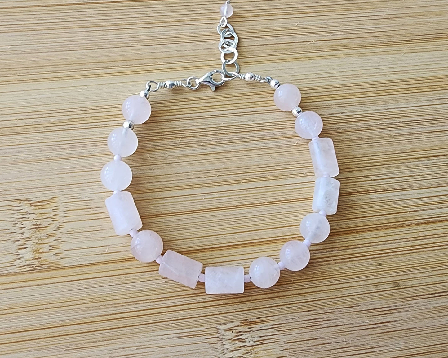 Rose Quartz PEACE bracelet, Morse Code spells the word PEACE with round and tube shaped pale pink Rose Quartz beads with Sterling Silver lobster claw clasp and extension chain, displayed on wood.