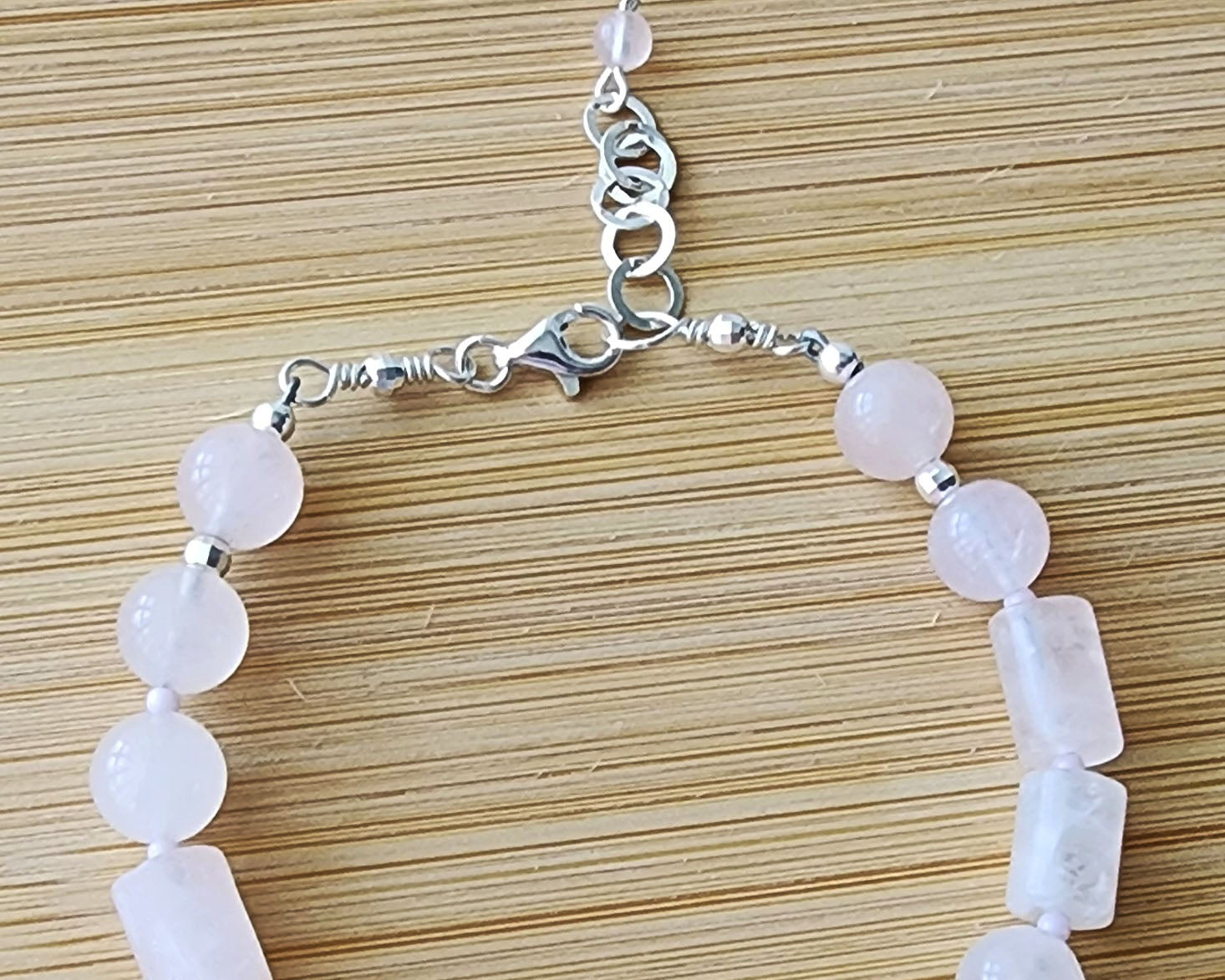 Rose Quartz PEACE bracelet, Morse Code spells the word PEACE with round and tube shaped pale pink Rose Quartz beads with Sterling Silver lobster claw clasp and extension chain, displayed on wood.