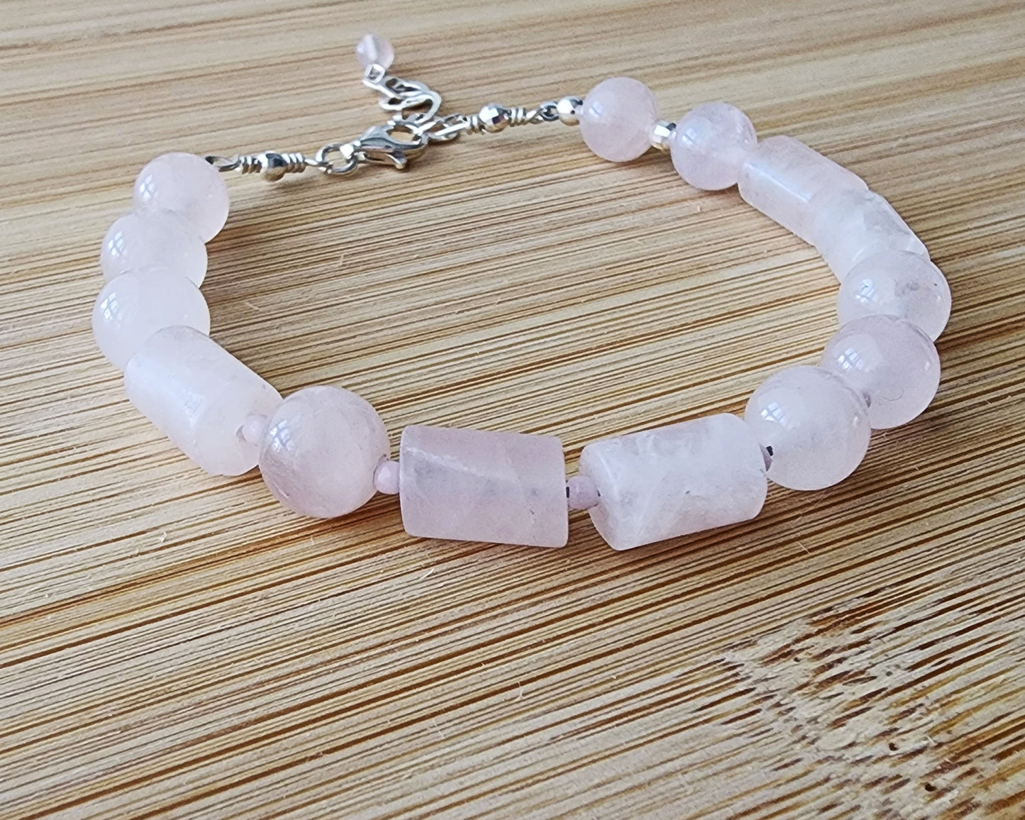 Rose Quartz PEACE bracelet, Morse Code spells the word PEACE with round and tube shaped pale pink Rose Quartz beads with Sterling Silver lobster claw clasp and extension chain, displayed on wood.