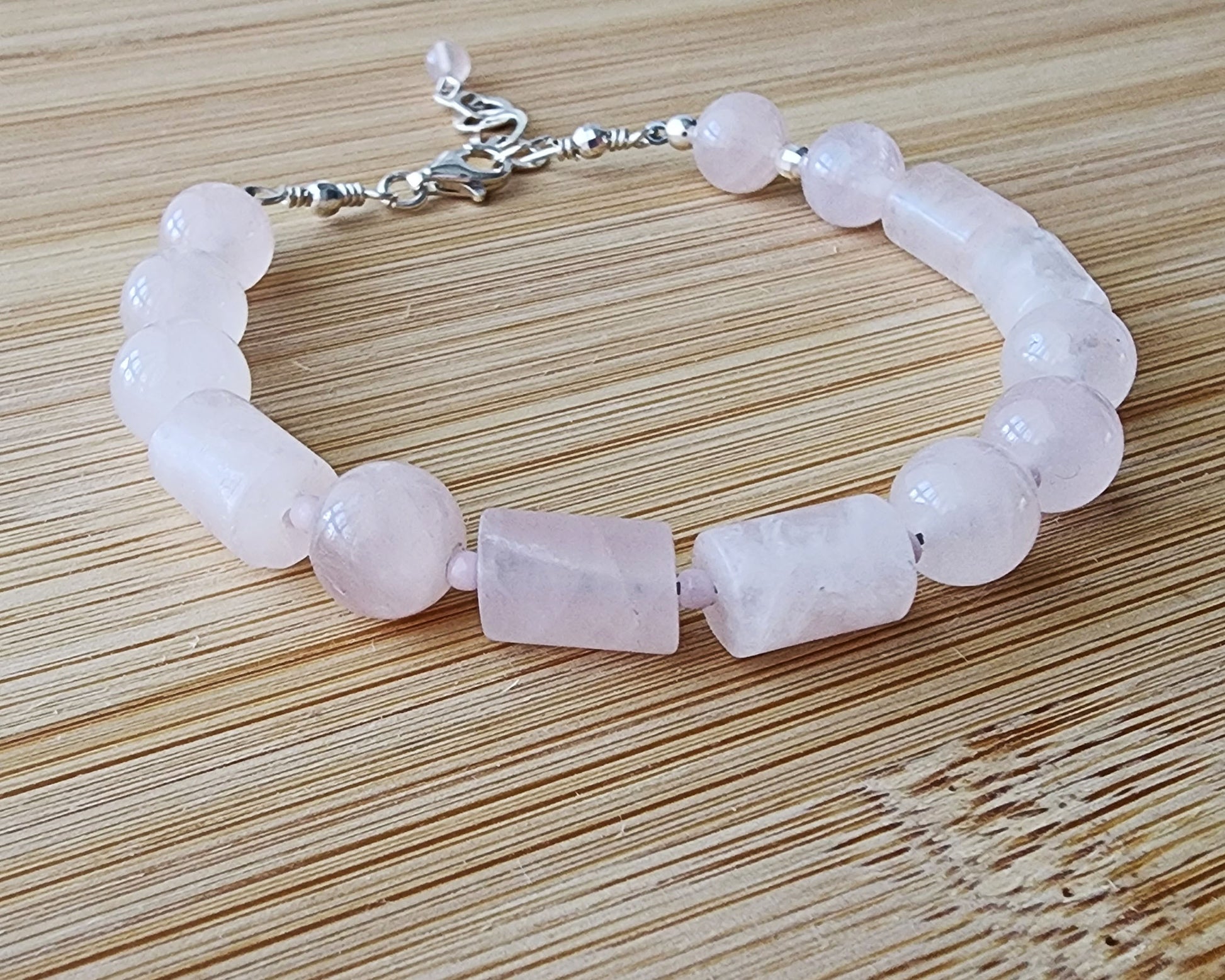 Rose Quartz PEACE bracelet, Morse Code spells the word PEACE with round and tube shaped pale pink Rose Quartz beads with Sterling Silver lobster claw clasp and extension chain, displayed on wood.