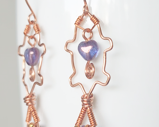A pair of wire wrapped copper beaver earrings with mauve purple hearts and tear drop stones on french hooks on wood 