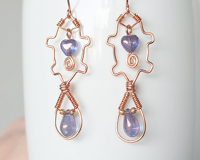 A pair of wire wrapped copper beaver earrings with mauve purple hearts and tear drop stones on french hooks on wood 