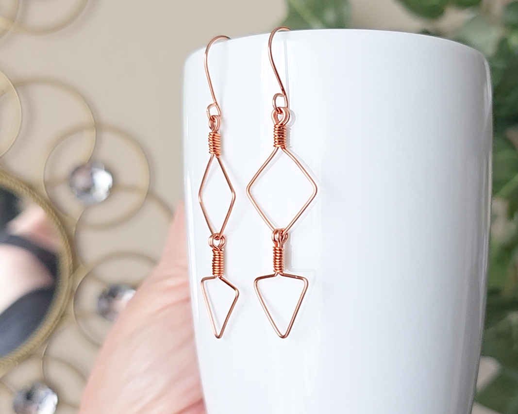 Long Geometric Copper Earrings with Square and Upside down triangles on french earring hooks displayed on white cup