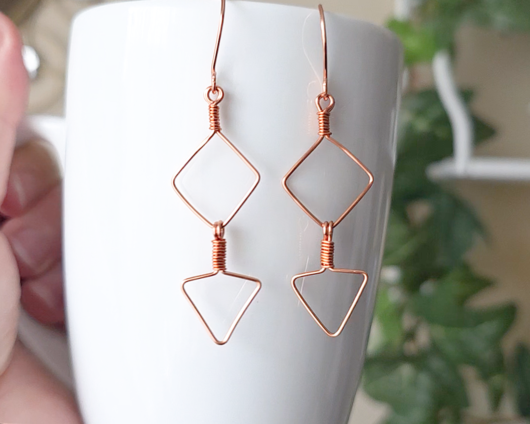 Long Geometric Copper Earrings with Square and Upside down triangles on french earring hooks displayed on white cup