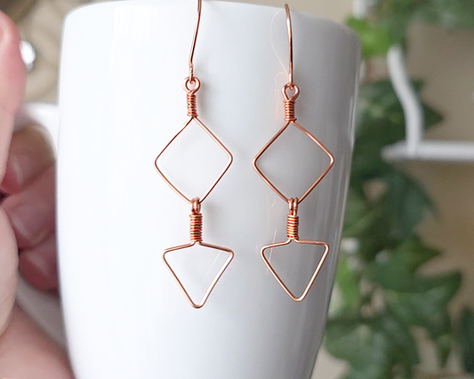 Long Geometric Copper Earrings with Square and Upside down triangles on french earring hooks displayed on white cup