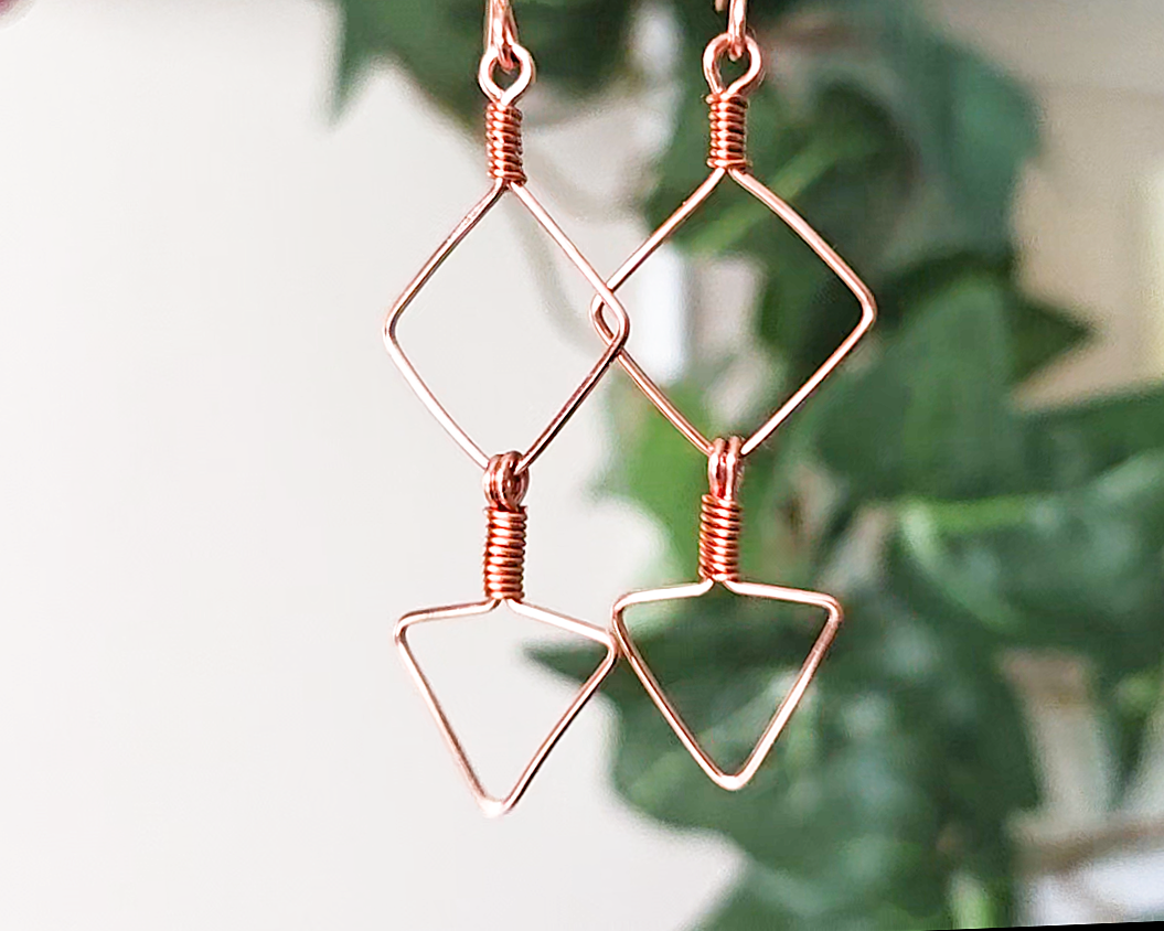 Long Geometric Copper Earrings with Square and Upside down triangles on french earring hooks with green plants in background