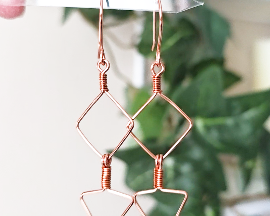 Long Geometric Copper Earrings with Square and Upside down triangles on french earring hooks with green plants in background