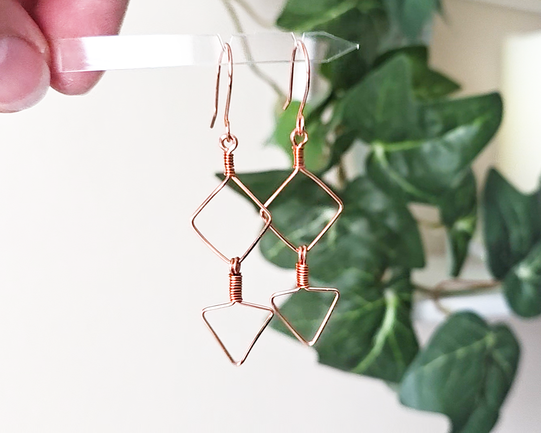 Long Geometric Copper Earrings with Square and Upside down triangles on french earring hooks with green plants in background