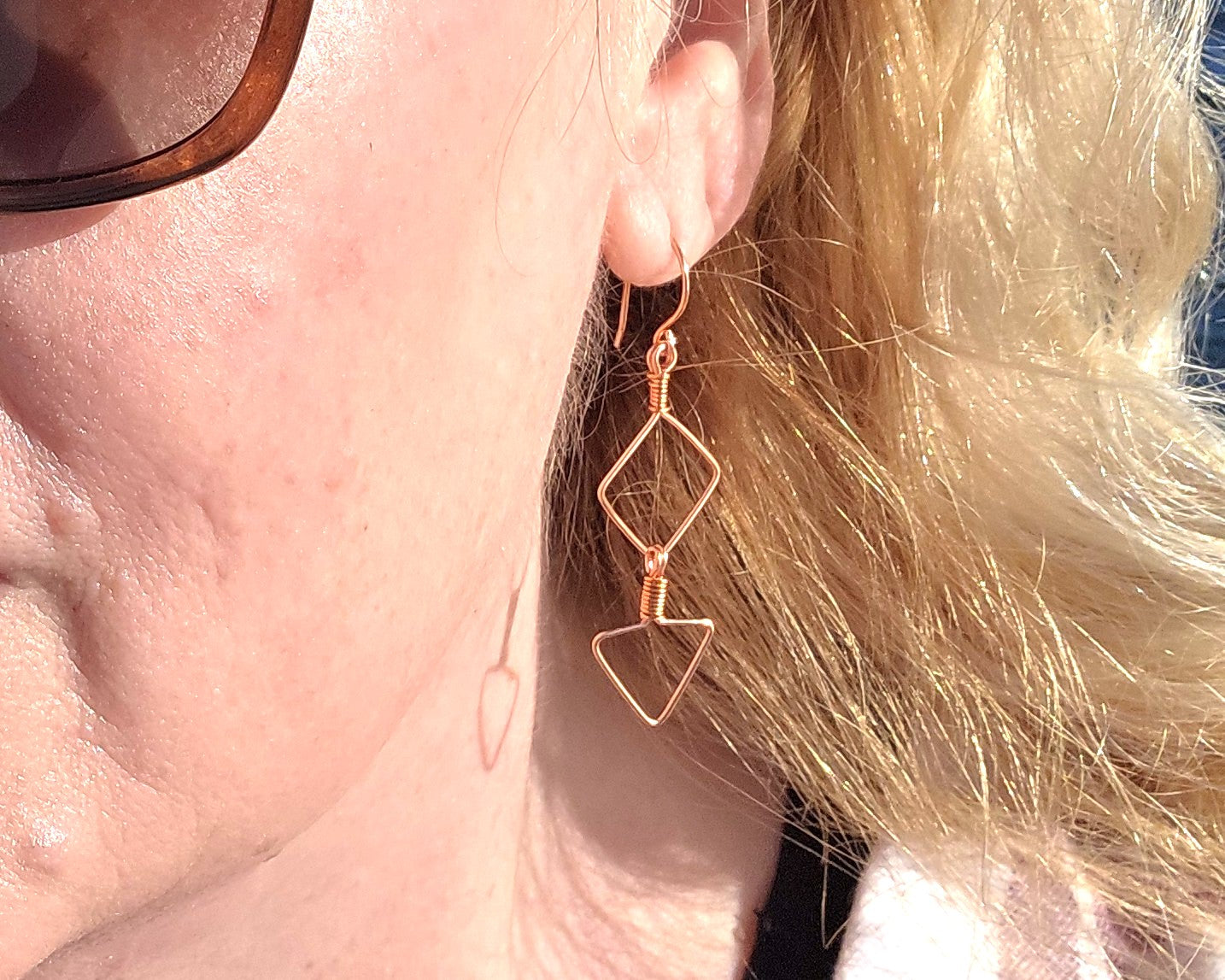 Close-up of a person wearing a geometric wire earring with blonde hair.