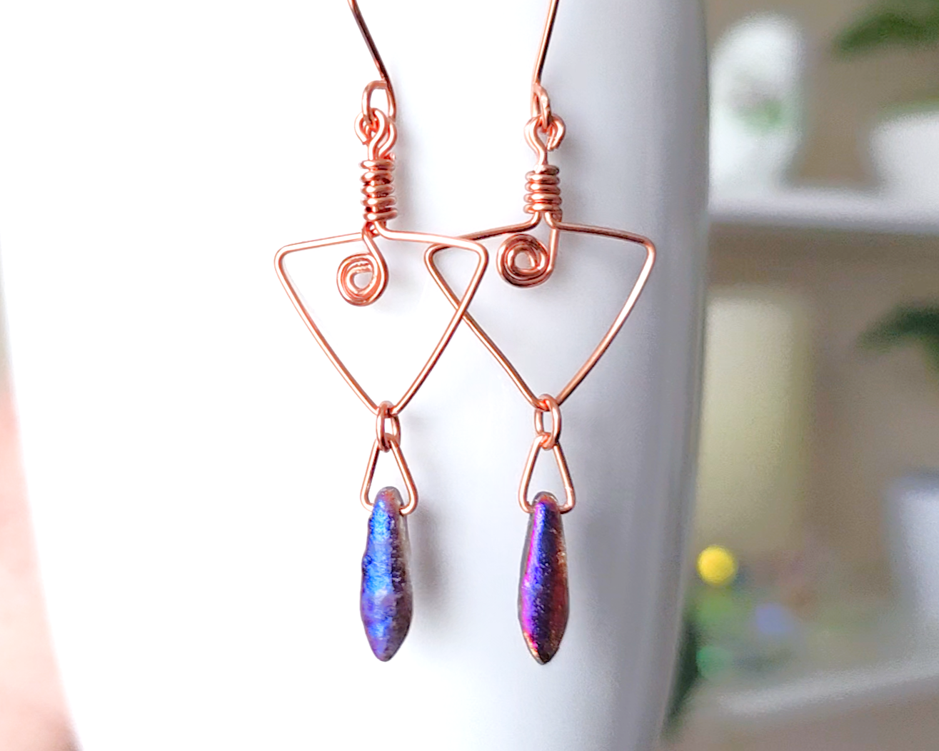 Long Copper Earrings with Celtic Coils in upside down triangle and dagger shaped Iridescent Purple Blue pendants dangling on the base displayed on white background