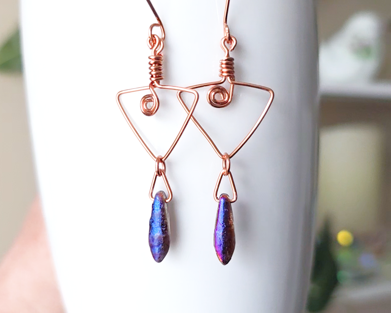 Long Copper Earrings with Celtic Coils in upside down triangle and dagger shaped Iridescent Purple Blue pendants dangling on the base displayed on white background