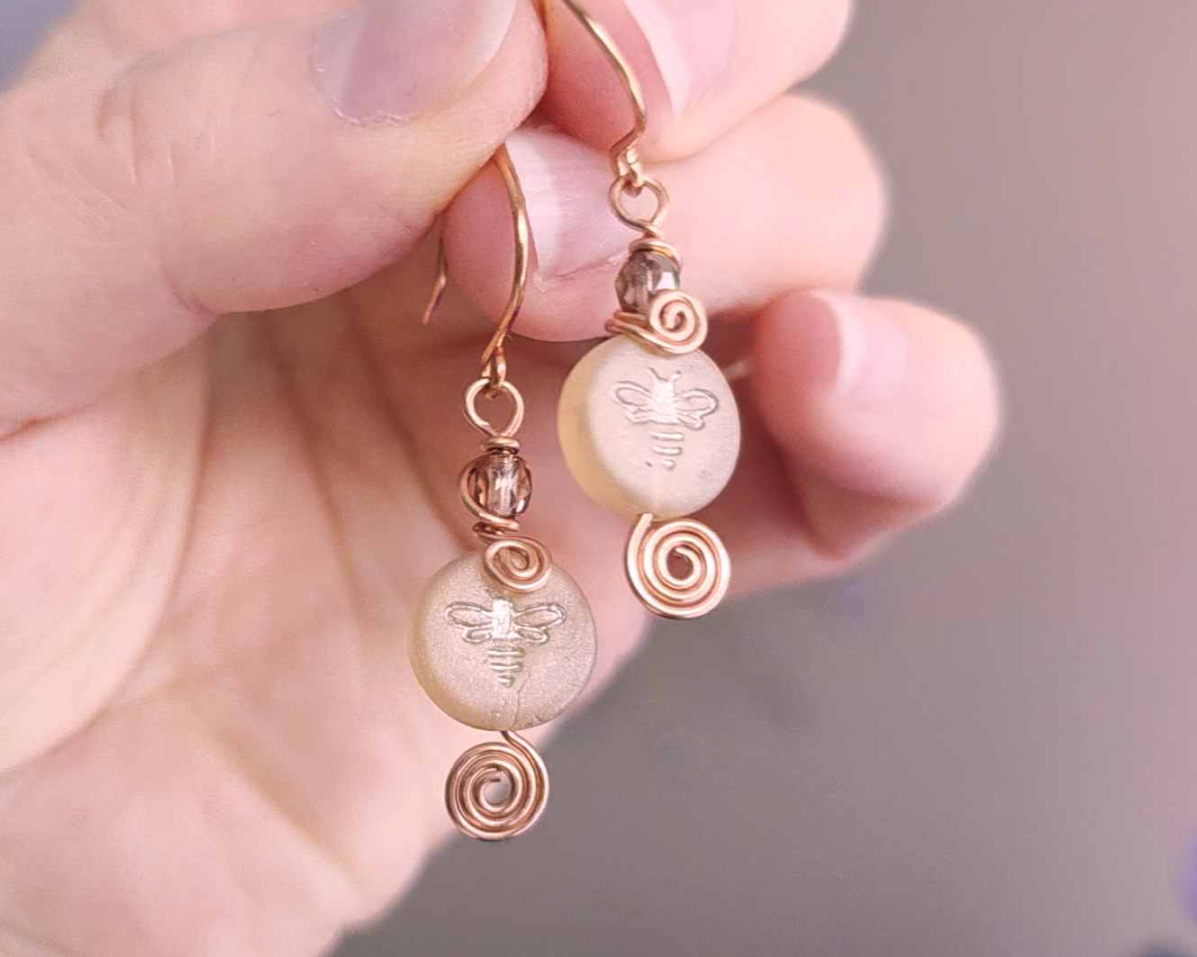 A pair of handmade copper and sparkly gold glass and round honey bee bead earrings with Celtic coils on french hooks in hand