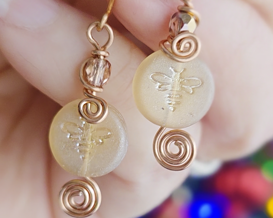 A pair of handmade copper and sparkly gold glass and round honey bee bead earrings with Celtic coils on french hooks in hand