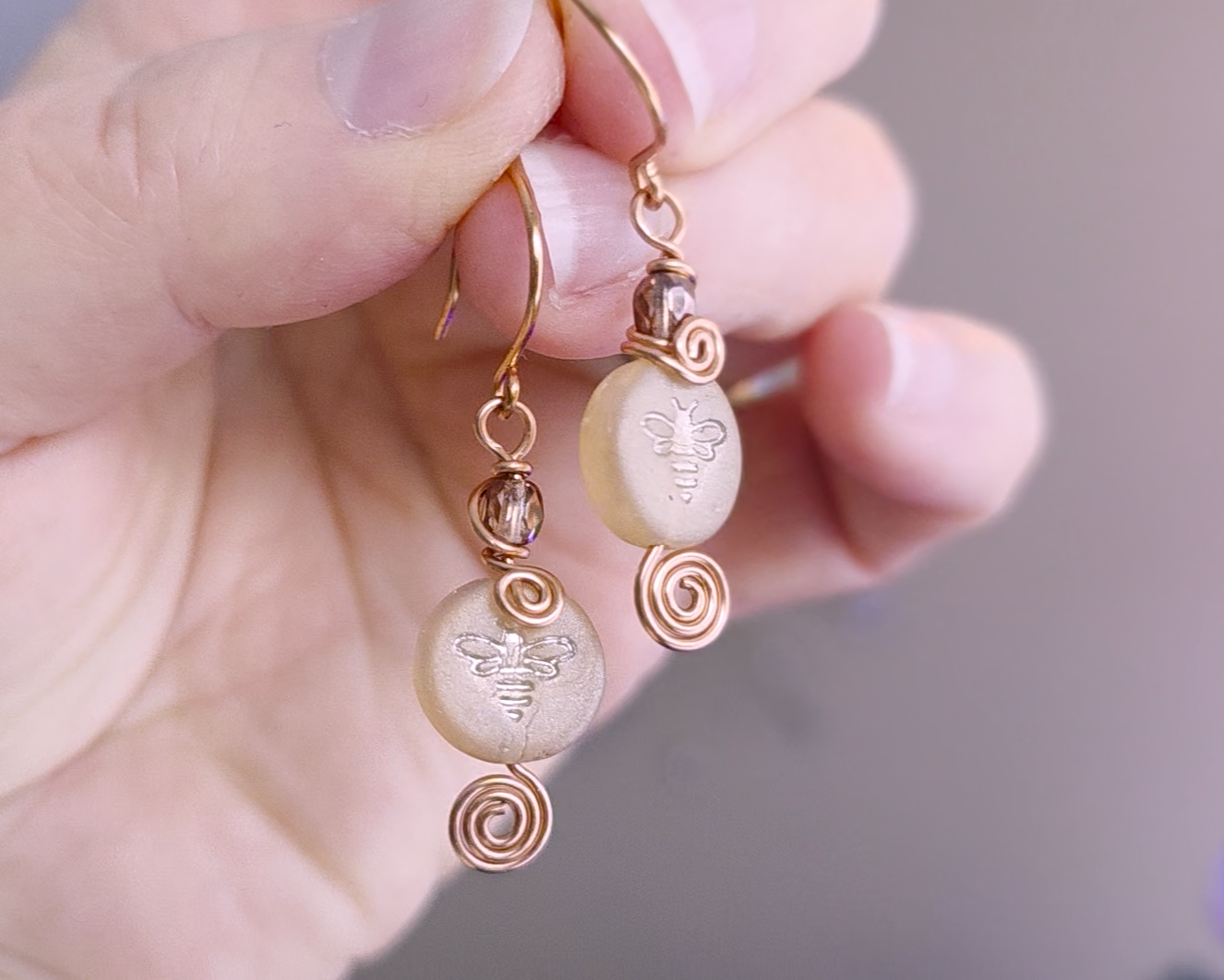 A pair of handmade copper and sparkly gold glass and round honey bee bead earrings with Celtic coils on french hooks in hand